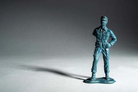 A small toy soldier figure stands upright with a confident pose. The soft lighting creates a