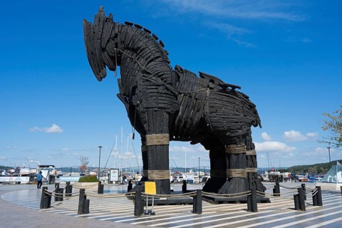 Wooden sculpture of a horse at the harbour in a clear, sunny environment with boats and clouds,
