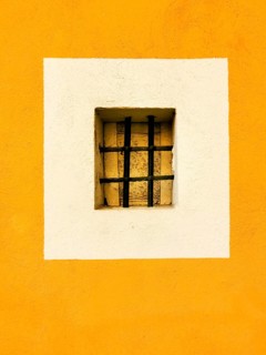 A small rectangular window with a black barred grille is centered in a white square, surrounded by