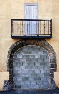 A metal-railed balcony stands over a blocked stone entrance on a textured yellow building, creating
