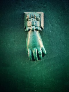 A unique green hand-shaped door knocker adorns a textured dark wall, adding a charming historical
