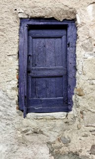 A small door painted in vibrant purple contrasts beautifully with a weathered stone wall. The