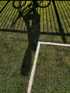 A cyclist casting a long shadow on vibrant green grass, creating a dynamic contrast with a white
