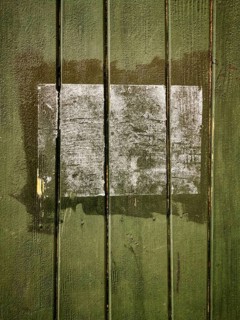 A rectangular patch on a green wooden surface shows faded remnants of a past application, with