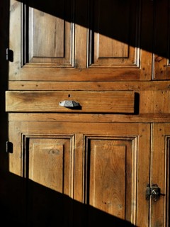 A vintage wooden cabinet features a prominent drawer, bathed in warm sunlight that casts shadows.