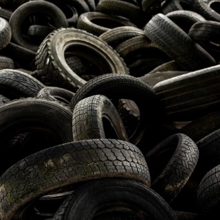 A large collection of worn-out tires is stacked chaotically in a junkyard, illustrating the