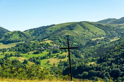 A wooden cross stands prominently against a picturesque landscape of rolling hills and vibrant