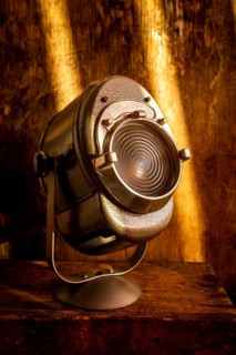 A vintage spotlight rests on a rustic wooden surface, casting a warm glow. Soft light enhances the