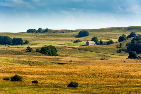 Lush green and golden fields extend across the landscape, with a quaint farmhouse nestled among