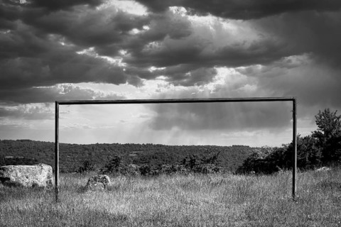 A solitary soccer goal stands in a grassy field under a moody sky filled with dark clouds. Puy de