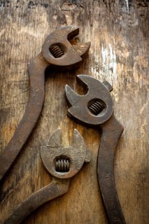 Three antique adjustable wrenches rest on a weathered wooden table, highlighting their unique