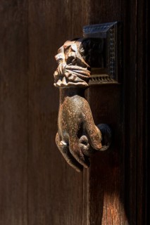 A detailed bronze hand-shaped door knocker is affixed to a rustic wooden door, showcasing intricate