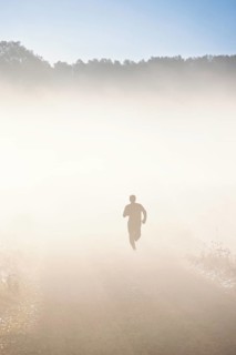 On person training running on a dirt road with morning fog in a rural landscape in autumn