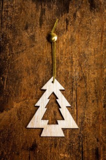 A handcrafted decoration shaped like a fir tree is suspended by a green string against a textured