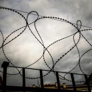 Rusty barbed wire coils twist against a dark and turbulent sky, creating a sense of confinement and