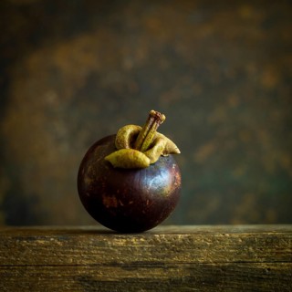 A ripe mangosteen sits gracefully on a weathered wooden surface, showcasing its dark purple skin