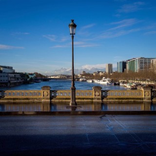 A street light stands tall on a bridge, casting light on the path as the serene Seine River flows