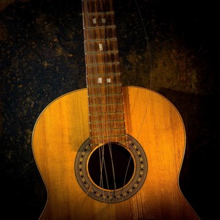 This classical guitar, resting against a dark brown backdrop, features broken strings that