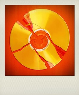 A broken polaroid compact disc lies on a bright red surface, showcasing multiple cracks radiating