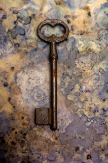 An old key lies against a blue and beige textured backdrop, showcasing its rust and wear. The key's