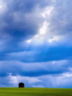 Nestled in a vibrant green field, a solitary hut stands against a backdrop of dynamic clouds,