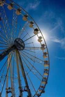 Bright sun shines behind a towering Ferris wheel, creating a vibrant atmosphere at an amusement