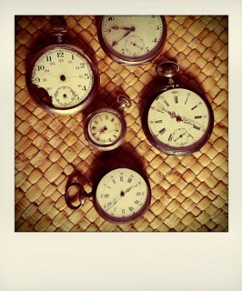 Various vintage stopwatches are displayed closely on a woven surface, highlighting their distinct