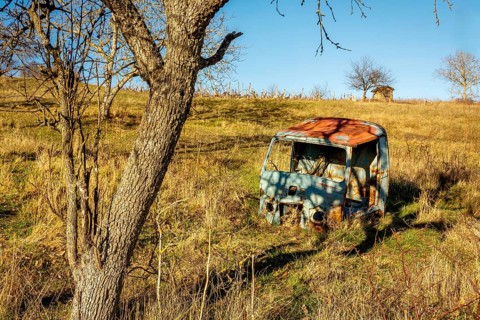 A weathered vehicle rests in a secluded field in Auvergne-Rhone-Alpes, France. Surrounded by tall