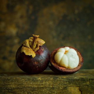 Two ripe mangosteens rest side by side, showcasing their deep purple skin. One fruit is cut in