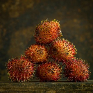 A cluster of rambutans sits on a wooden surface, highlighting their unique hairy skin and rich