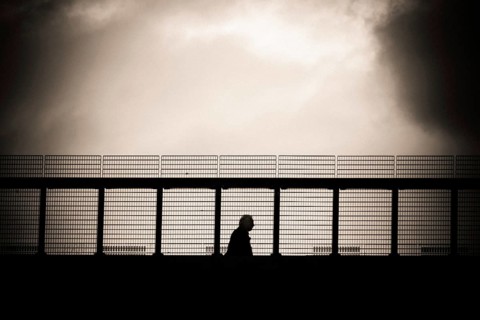 A solitary figure walks along a metal gangway in Lausanne, Switzerland, with a dramatic cloudy sky
