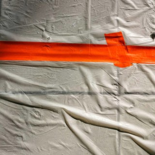 Bright orange tape stretches across a wrinkled white surface, creating a clear boundary. This setup