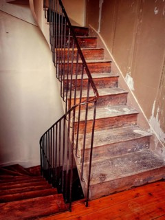 A winding staircase constructed from rustic wood features elegant iron railings, set in a partially