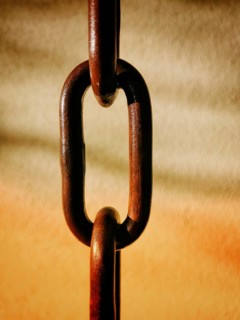 Close-up of a rusty chain with interlocking links suspended against a softly blurred warm backdrop.