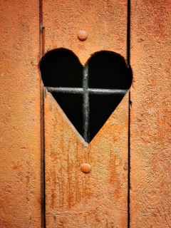 A rustic wooden door features a heart-shaped cutout that reveals iron bars behind it. The warm