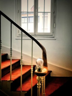A staircase is gracefully illuminated by a soft light bulb on the railing, leading upward with a