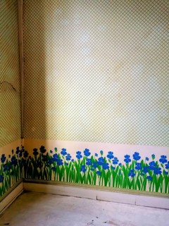 An empty corner room features a unique wall design, showcasing vibrant blue flowers and green grass