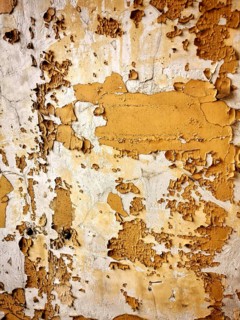 This textured wall features layers of peeling paint in warm yellow and beige tones, revealing the