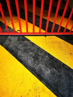 Bright yellow and black stripes intersect with a bold red barrier across a concrete surface. This