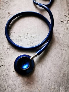 A blue stethoscope lies on a textured surface, its reflection catching the light in a clinical