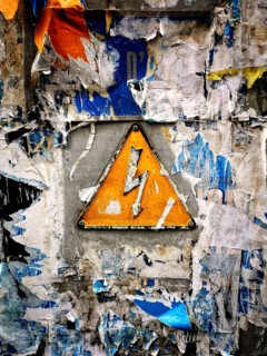 A bright yellow warning sign featuring a lightning bolt is mounted on a wall heavily covered with