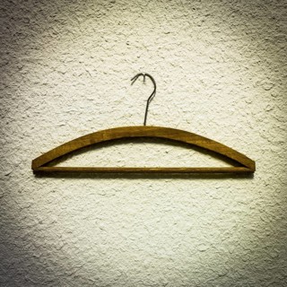 Wooden hangers are displayed against a textured light wall, highlighting a minimalist approach to