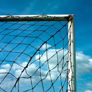 A football goal net is positioned against a cloudy sky, showcasing the intricate details of the