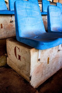 Rows of empty blue seats rest on a weathered concrete base in a deserted sports arena, highlighting