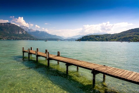 Clear skies reflect on the calm waters of Annecy lake, while a wooden pontoon invites visitors to