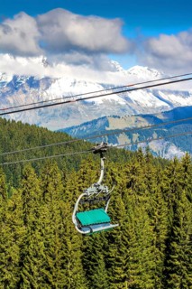 A ski lift transports visitors above green forests toward snowy mountain peaks in Haute-Savoie,