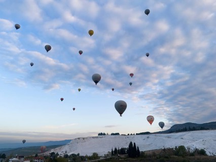 Hot air balloons float over a picturesque landscape under a cloudy sky, aerial view, Pamukkale,