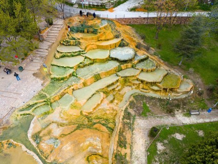 Multicoloured natural mineral terraces with water accumulations in a park landscape, aerial view,
