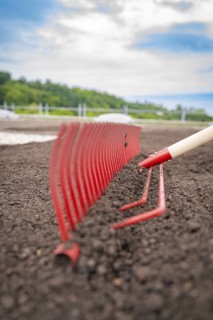 Close-up of a red rake working the soil on a roof, with nature in the background, roof greening,