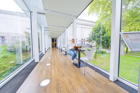 Woman sitting in a bright café with glass walls and a green garden view, Frieder Burda Museum,